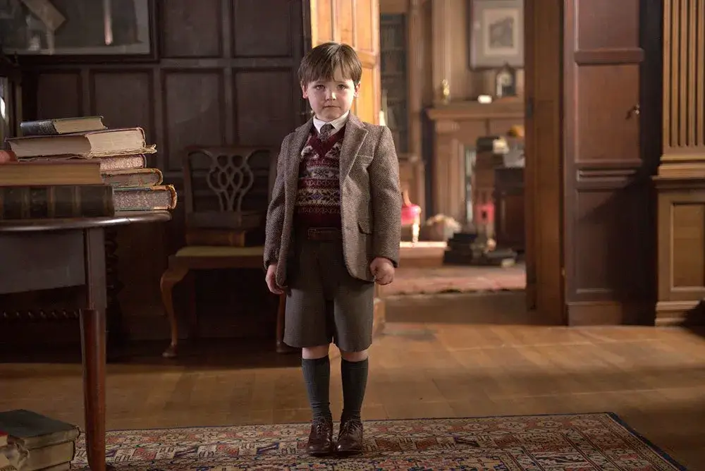 Roger Wakefield enfant vêtue d'une tenue élégante, se tenant dans le salon du Révérand Wakefield. - Outlander saison 2 épisode 1 : "A travers le miroir"