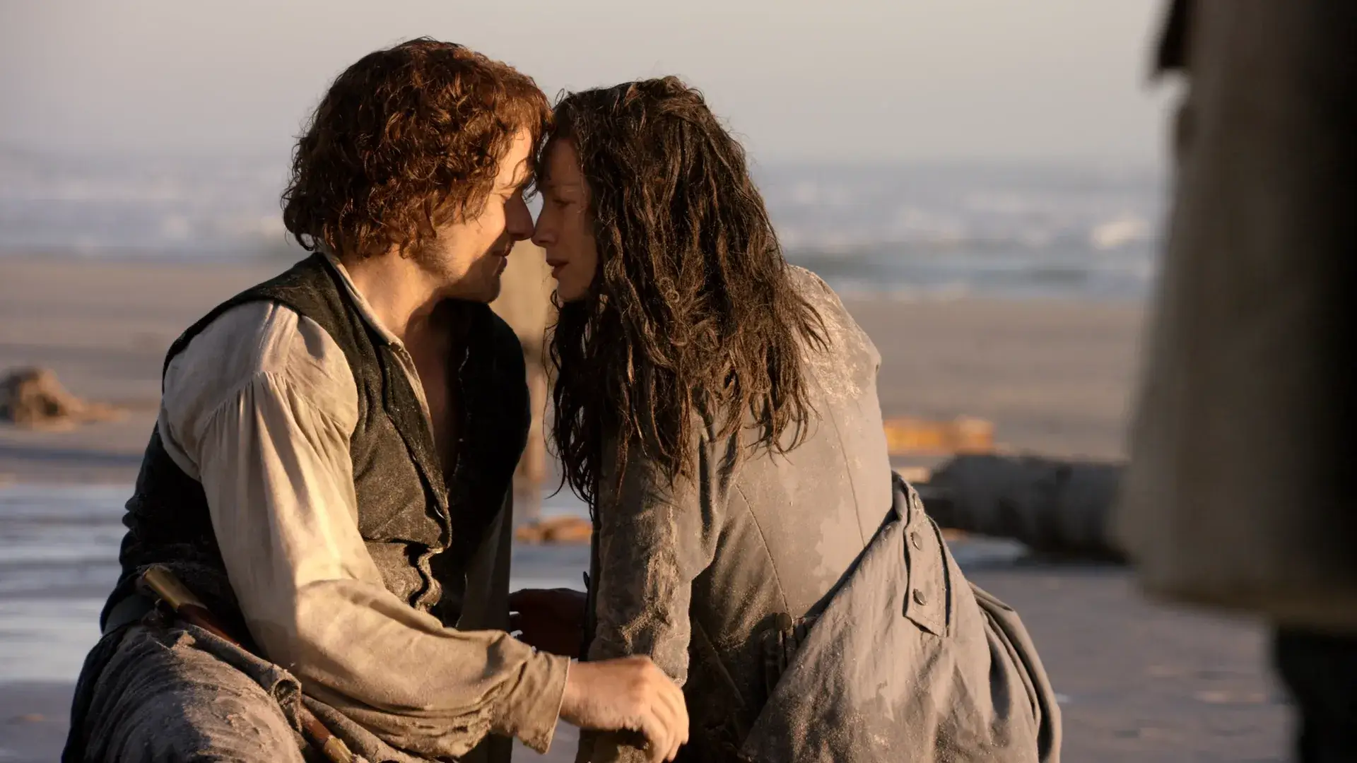 Claire et Jamie Fraser retrouvent refuge l’un auprès de l’autre sur la plage, sales et épuisés après un naufrage – scène forte d’Outlander saison 3.