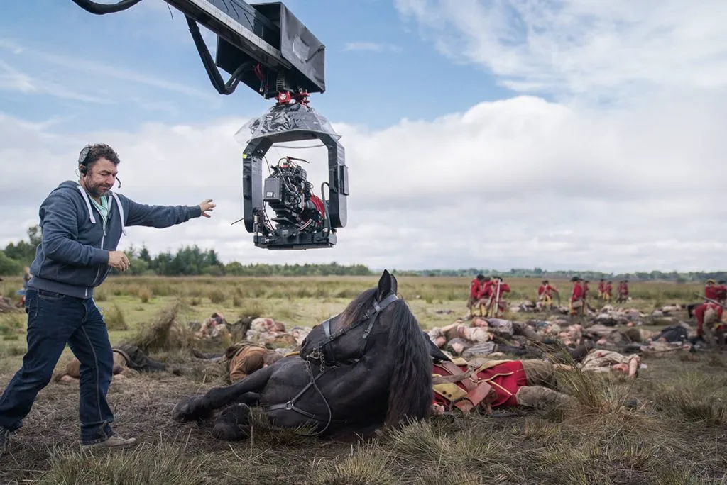 Un caméraman film le massacre de Culloden. Un cheval noir se trouve au premier plan avec de nombreux soldats Jacobite morts. On aperçoit quelques soldats britaniques à l'arrière plan. - Outlander saison 3 épisode 1 "A chacun son combat"