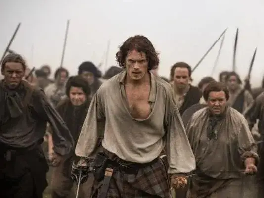 Jamie Fraser menant une charge armée aux côtés des Highlanders, symbolisant la rébellion jacobite dans la série Outlander.